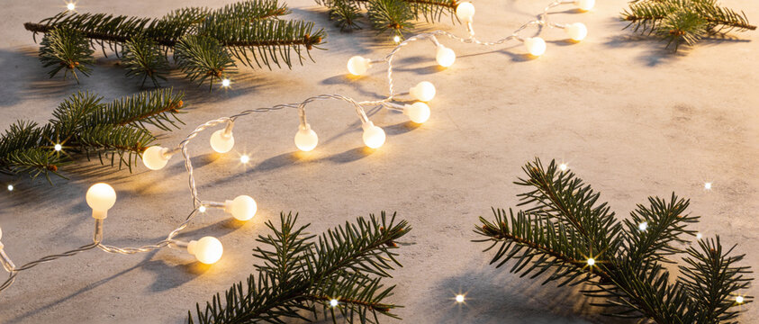 Warm fairy lights and pine branches lying on a bed of white snow, illuminating a festive winter scene.