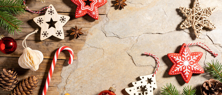 Flat lay of Christmas decorations including candy canes, wooden stars, and pine cones on a rustic stone and wood background
