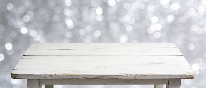 White wooden table top with a bright silver bokeh background, featuring large white copy space below.