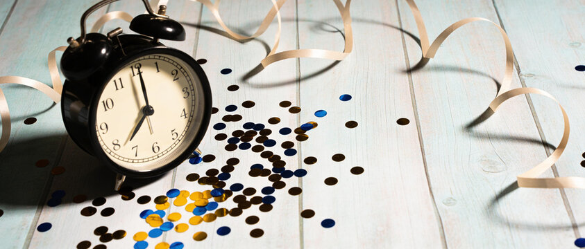 Black alarm clock with scattered colorful vitamin tablets and spiral strips on a light blue wooden table surface.