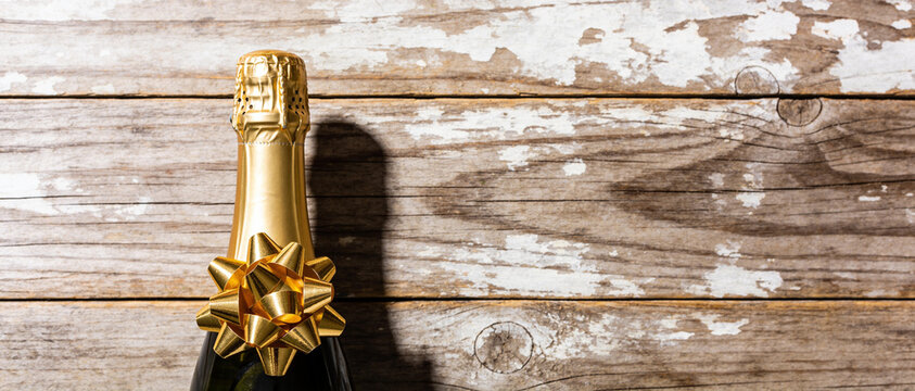 The top of a champagne bottle with a gold foil neck and bow resting on a rustic white wooden surface