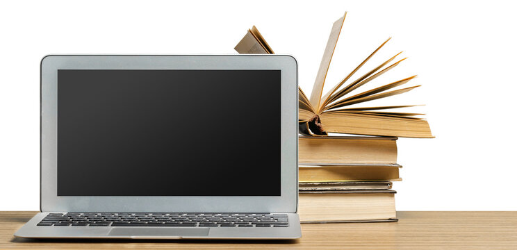 Laptop beside a stack of open and closed books on a wooden table