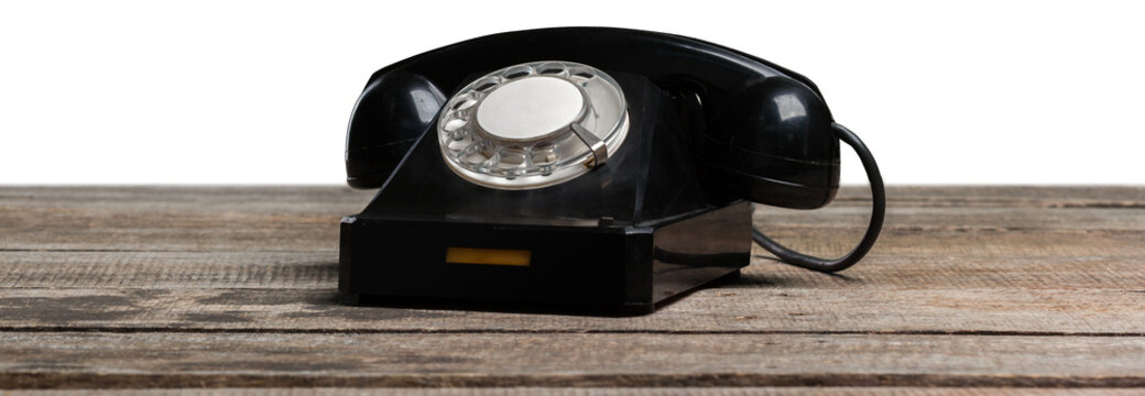 Old black rotary telephone on wooden table in a bright light setting