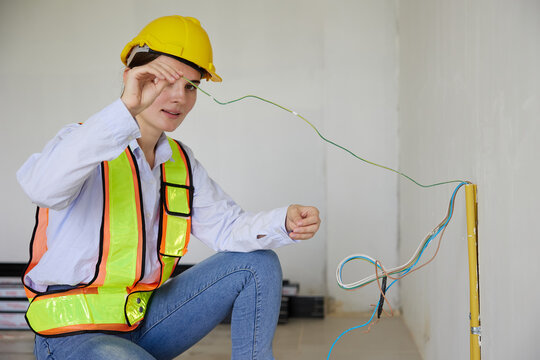 Female construction worker crouching and examining electrical wires on a construction site