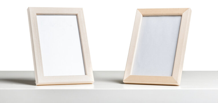 Two empty picture frames on a white shelf arranged at a slight angle facing each other