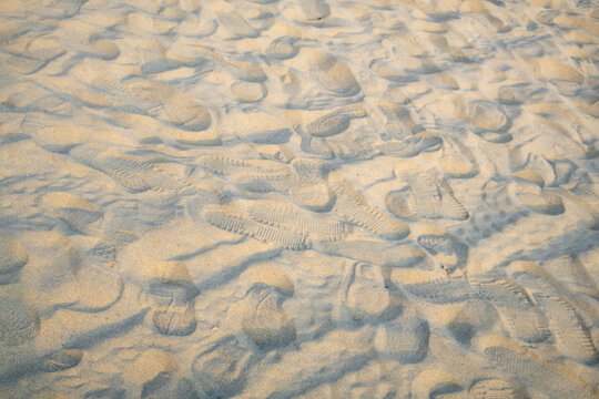 Numerous footprints and shoe tracks imprinted on fine beach sand