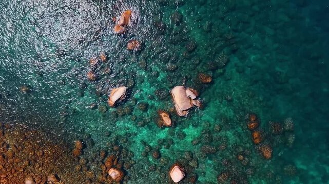 Exposed boulders interrupt the rippled surface of Lake Tahoe. An overhead view shows brown rocks through green water with white reflections across the upper left.
