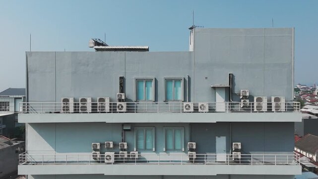 Aerial view of a modern building facade featuring numerous air conditioning units mounted on balconies under a clear blue sky in Malang, East Java, Indonesia.
