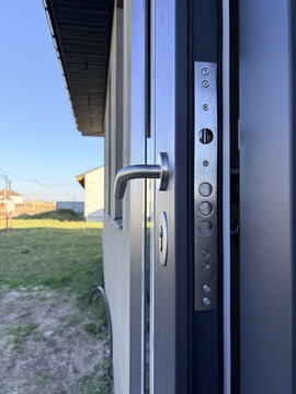 Side view of a modern grey entrance door featuring a multi-point locking system and silver handle. Home security, construction, renovation, architectural hardware, and safety.