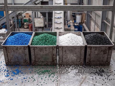 Recycled plastic pellets sorted by color in metal bins at a plastic recycling plant