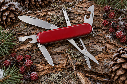 Red multi tool knife open on tree bark background with pine cones and berries, outdoor adventure gear, survival equipment, camping concept.