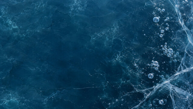 Dark blue frozen pond ice with cracks and trapped bubbles