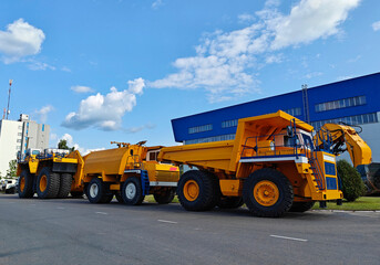 Smalyavichy, Belarus - June 14, 2025: Belaz huge dump trucks parked in industrial area with blue building © Slepitssskaya