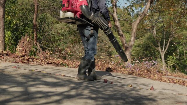 Worker Using a Leaf Blower to Clear Autumn Leaves from a Path