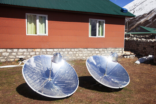 Solar cookers are featured in a sunny outdoor area near a house in the mountains during the day