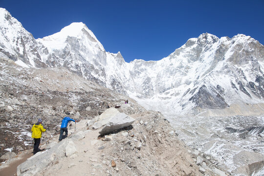 Hikers explore the Mount Everest region with snow-capped peaks and rocky terrain on a clear day in spring