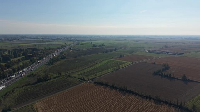 Aerial View of Rural Landscape: An expansive drone shot captures a vast rural landscape, featuring patchwork fields, a distant farmhouse, and a highway with a gentle curve under a clear blue sky.