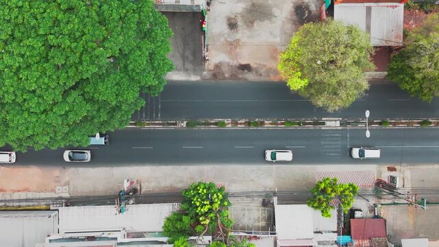 Malang, East Java, Indonesia - 12 October 2026: Aerial view of a street with cars driving along the road, lined with lush green trees and urban buildings.