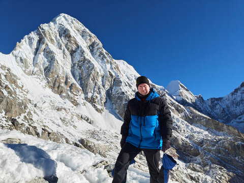 Hiker stands on snowy mountain trail near high peaks during clear day in winter season