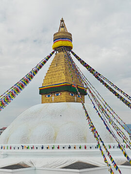 Buddhist stupa stands tall with colorful prayer flags flying in the breeze near Boudhanath in Kathmandu during an overcast day