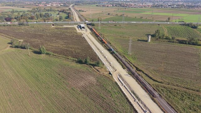 Aerial view of a rail freight service carrying maritime containers across cultivated fields in northern Italy.