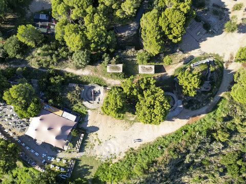 Aerial view of historic coastal fortifications and bunkers surrounded by pine trees and a restaurant terrace in Montgat, Catalonia, Spain.