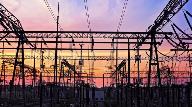Silhouette of an electrical substation and high-voltage power transmission lines at sunset