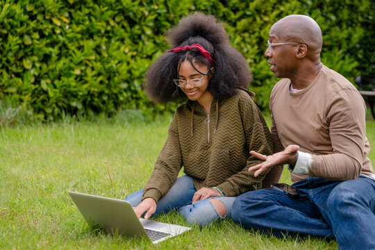 Father and daughter use laptop together on grass in their backyard