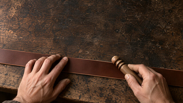 Hands burnishing brown leather strap with wooden slicker tool