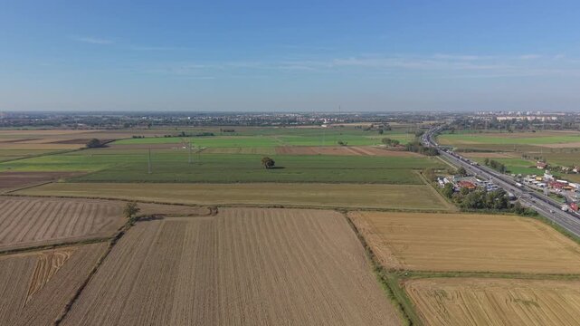 Rural Panorama: An aerial view showcases a patchwork of cultivated fields stretching towards a distant highway and urban silhouette under a clear blue sky.