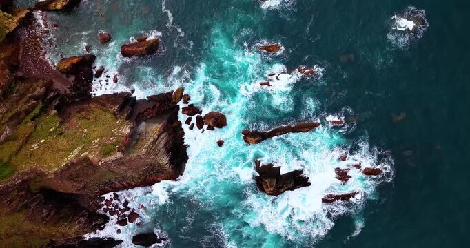 Abstract aerial top-down shot of rough ocean water and waves breaking against coastal rocks in Moniello, Northern Spain.