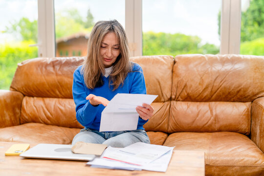 Woman sitting on a brown couch reading letters with a worried expression at home
