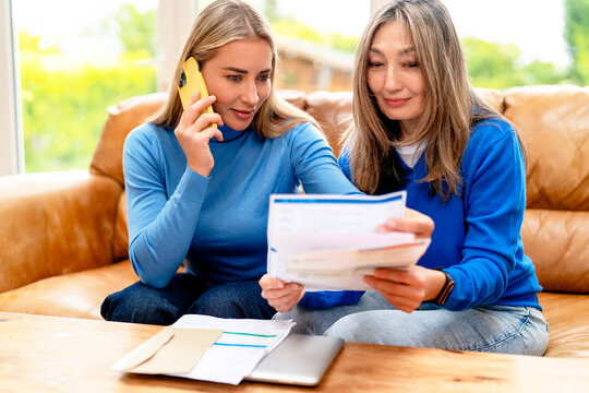 Two women discussing documents while on the phone in a cozy living room during daytime