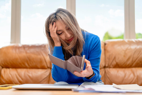 Woman holding empty wallet while sitting on a couch indoors with a worried expression at home