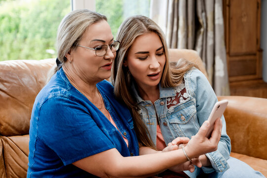 Two women looking at a smartphone while sitting on a couch in a living room during the daytime