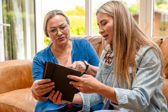 Two women look at a tablet together in a bright living room in afternoon light