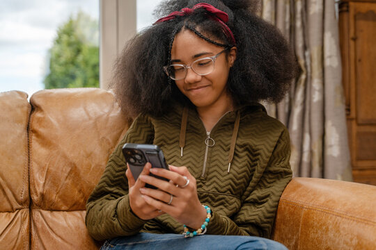 Young girl sitting on a couch looking at her smartphone with a smile in a cozy room