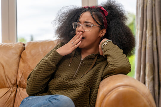 Girl yawning while sitting on a couch in a living room during the day