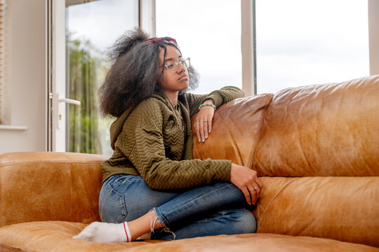 Young person sitting alone on a sofa in a room with large windows during the day