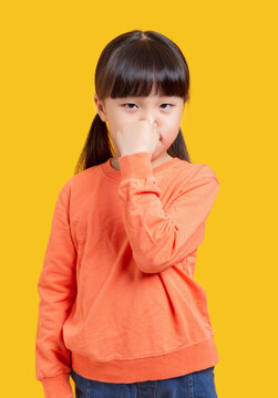 Cute Asian schoolgirl pinching nose, child reacting to bad smell on yellow background, disgust and hygiene concept