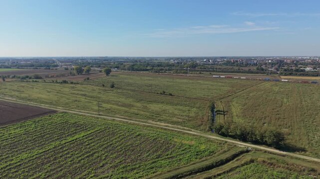 Aerial view of a freight train transporting intermodal shipping containers through agricultural fields in Lombardy, Italy.