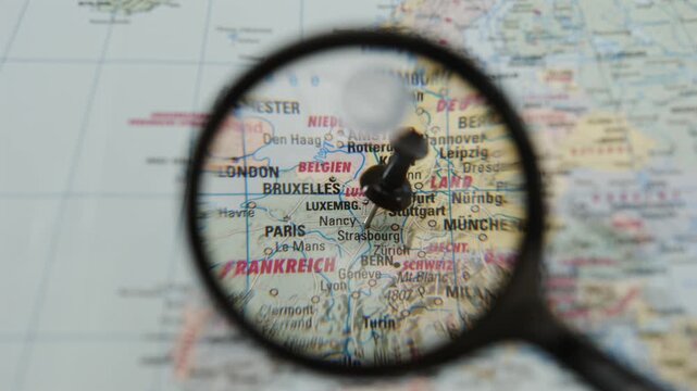 Printed European map centers on Strasbourg beneath magnifying glass, while dark location pin marks area. Map research helps travelers consider routes across neighboring countries and examine city