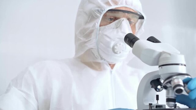 Scientist in ppe analyzing samples using a microscope in a laboratory setting