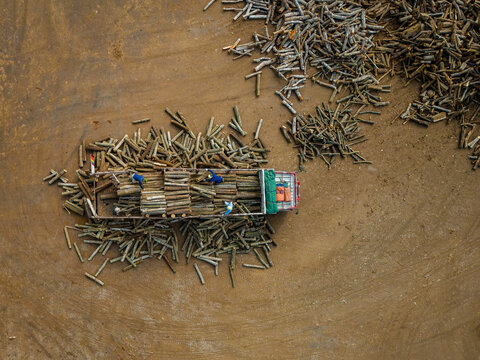 Aerial view of workers loading logs onto a truck in a large dirt yard in Boyolali, Central Java, Indonesia.