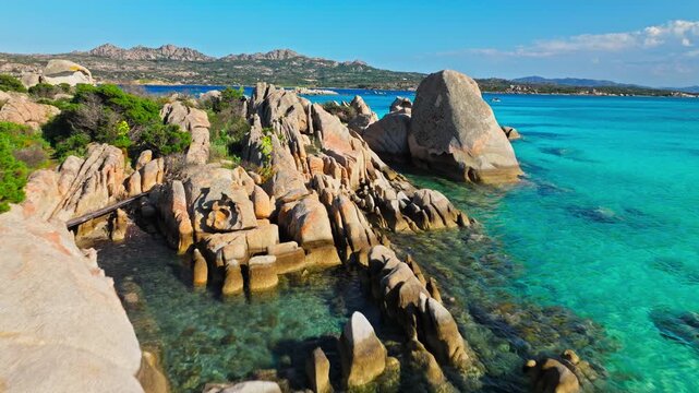 Ground view of Spiaggia Testa del Polpo in La Maddalena. Massive granite rocks, blue Mediterranean water and rugged coastline create a dramatic island beach scene.