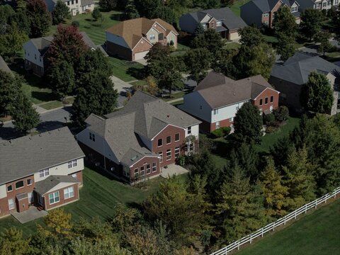 Aerial view of a suburban residential neighborhood featuring detached houses with brick and siding facades, manicured lawns, mature trees, and a white fence in Mason, Ohio, United States.