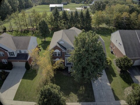 Aerial view of suburban residential houses with brick facades, driveways, and green lawns surrounded by trees in a neighborhood in Mason, Ohio, United States.