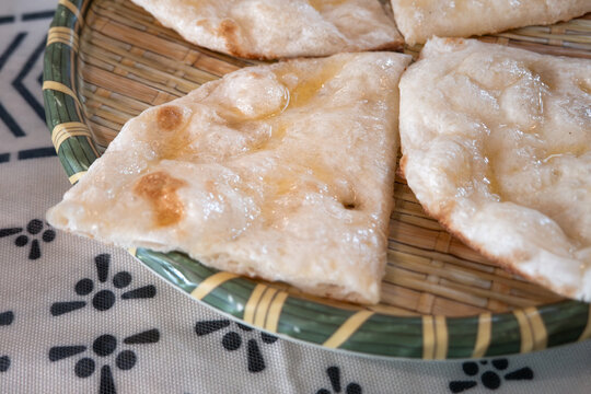 Fresh baked Indian naan flatbread slices served on a woven plate.