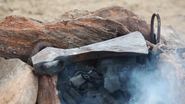 Axe head heating over glowing coals in a traditional forge