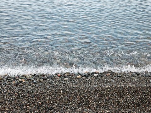 Small waves breaking on a pebble beach. Clear ocean water washing over smooth stones on the shore